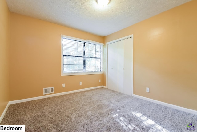 unfurnished bedroom featuring a textured ceiling, carpet flooring, and a closet