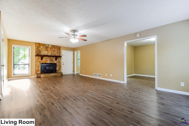 unfurnished living room with a textured ceiling, a stone fireplace, dark wood-type flooring, and ceiling fan