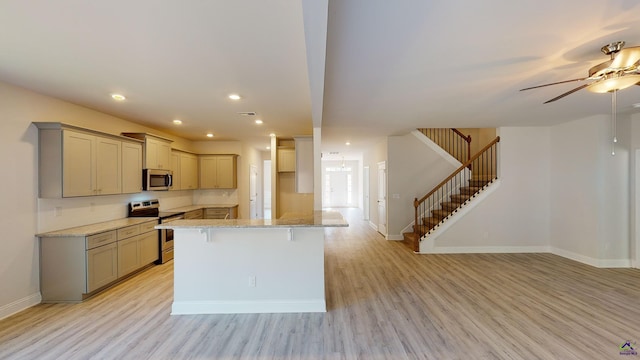 kitchen featuring a breakfast bar, light hardwood / wood-style flooring, appliances with stainless steel finishes, light stone countertops, and ceiling fan