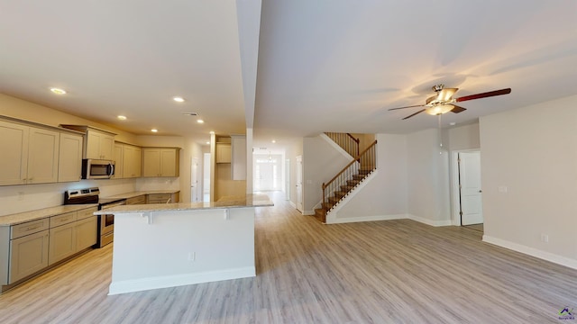 kitchen with a breakfast bar, light stone countertops, stainless steel appliances, ceiling fan, and light hardwood / wood-style flooring