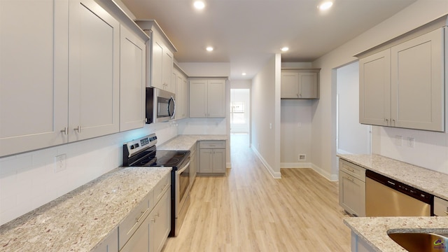 kitchen with gray cabinetry, light stone countertops, stainless steel appliances, light hardwood / wood-style flooring, and sink