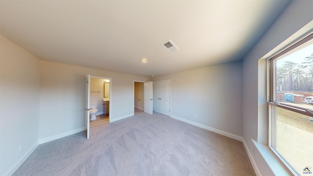 unfurnished bedroom featuring light carpet, a closet, and ensuite bathroom