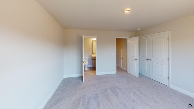 unfurnished bedroom with light colored carpet, a closet, and ensuite bath