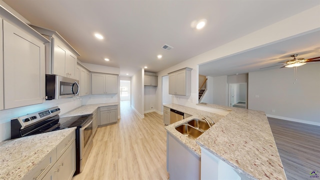 kitchen featuring light hardwood / wood-style floors, light stone counters, stainless steel appliances, ceiling fan, and sink