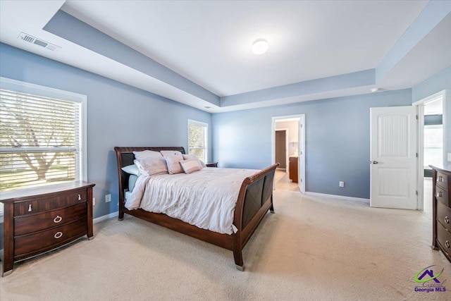 carpeted bedroom featuring multiple windows, ensuite bath, and a raised ceiling