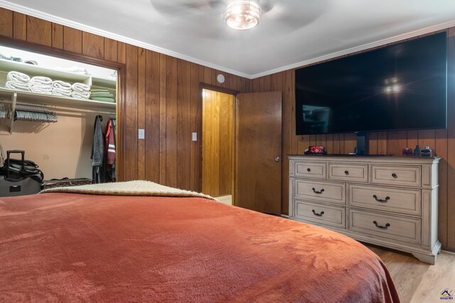 bedroom with wooden walls, light hardwood / wood-style floors, ornamental molding, and ceiling fan