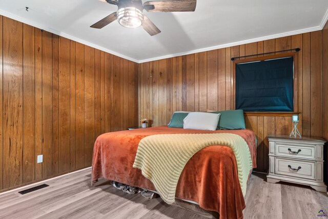 bedroom featuring ceiling fan, light wood-type flooring, crown molding, and wood walls