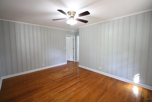spare room with wood finished floors, a ceiling fan, baseboards, and crown molding