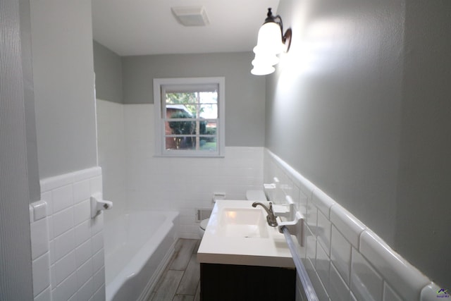 bathroom with tile walls, vanity, wainscoting, a bath, and wood finished floors