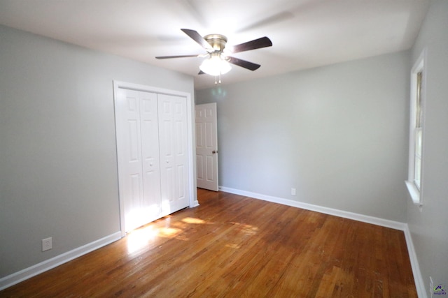 unfurnished bedroom with wood finished floors, a closet, baseboards, and a ceiling fan