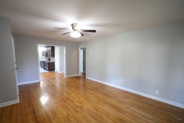 empty room with a ceiling fan, light wood finished floors, and baseboards