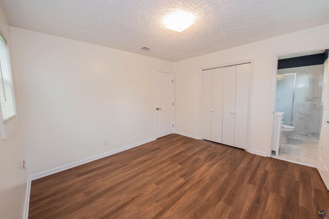 unfurnished bedroom with a textured ceiling, a closet, dark hardwood / wood-style floors, and ensuite bathroom