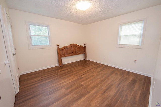 unfurnished bedroom with a textured ceiling and dark wood-type flooring