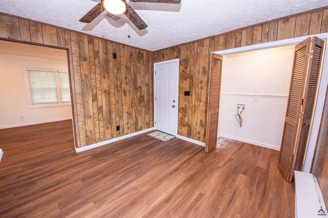 unfurnished bedroom featuring a closet, a textured ceiling, dark hardwood / wood-style floors, wood walls, and ceiling fan