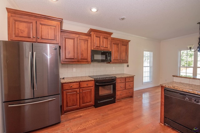 kitchen featuring light stone countertops, light wood-type flooring, decorative backsplash, black appliances, and ornamental molding