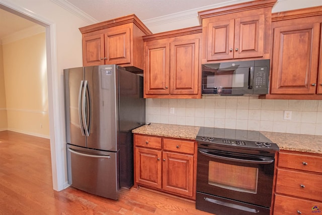 kitchen featuring light wood-type flooring, tasteful backsplash, light stone counters, ornamental molding, and black appliances