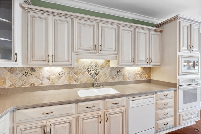 kitchen with cream cabinetry, backsplash, sink, and white appliances