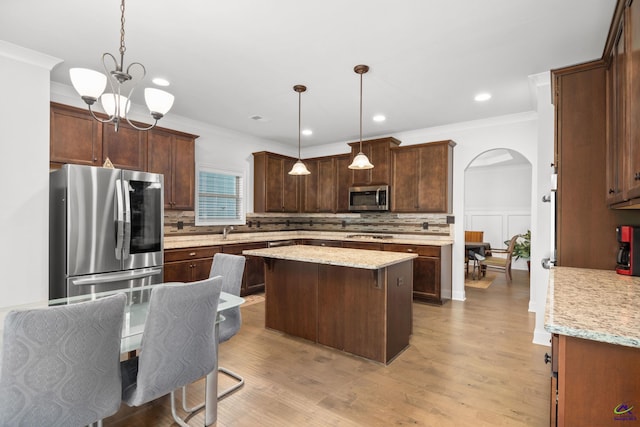 kitchen with pendant lighting, backsplash, appliances with stainless steel finishes, and light wood-type flooring