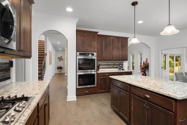 kitchen with hardwood / wood-style floors, crown molding, hanging light fixtures, appliances with stainless steel finishes, and backsplash