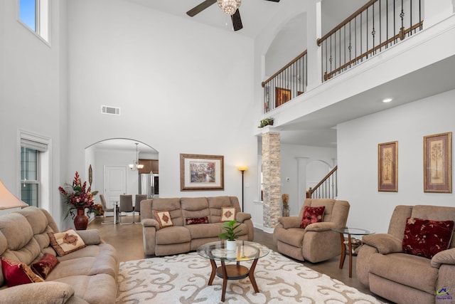 living room featuring wood-type flooring, ceiling fan with notable chandelier, and a high ceiling