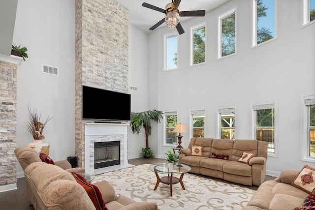 living room featuring ceiling fan, a high ceiling, a wealth of natural light, and a stone fireplace