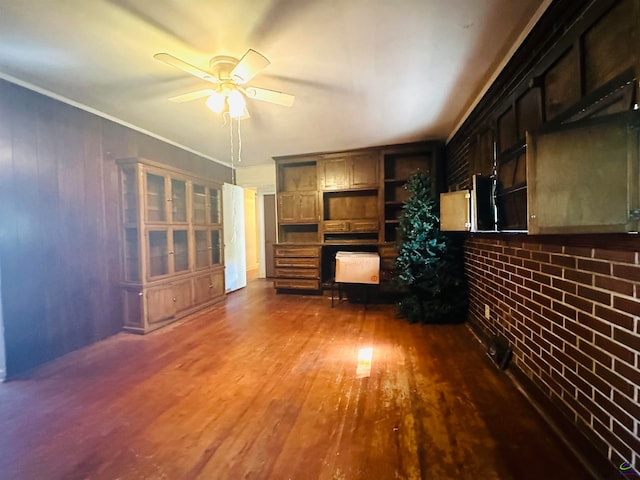 unfurnished living room with brick wall, dark wood-type flooring, crown molding, and ceiling fan