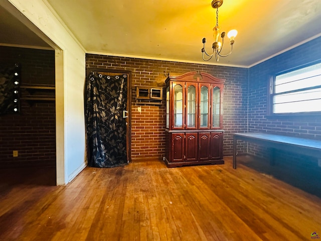 unfurnished dining area with brick wall, ornamental molding, and hardwood / wood-style floors