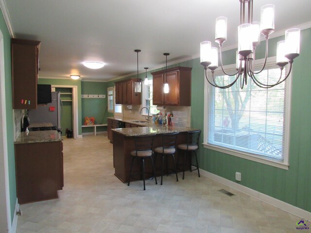 kitchen with sink, stone countertops, kitchen peninsula, hanging light fixtures, and an inviting chandelier