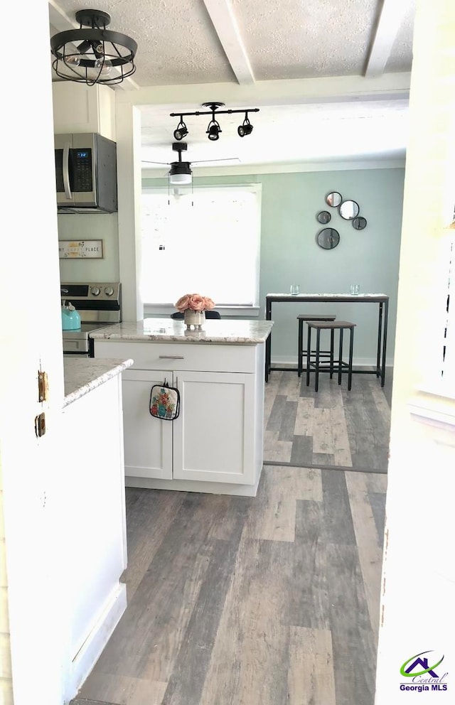 kitchen with white cabinets, beam ceiling, light stone counters, dark hardwood / wood-style floors, and stainless steel appliances