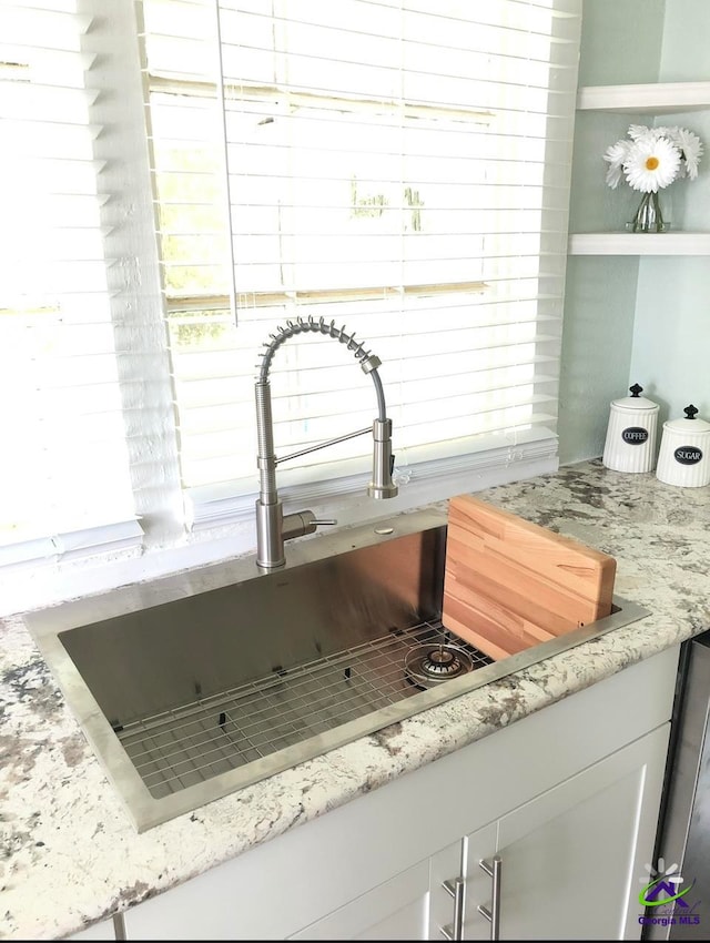 room details with light stone countertops, sink, and white cabinets