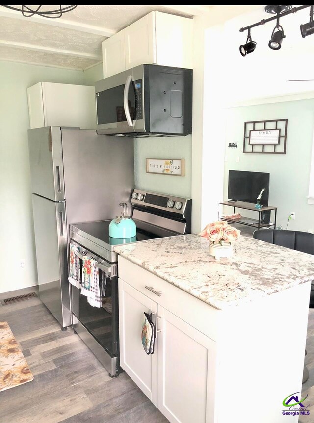 kitchen with light wood-type flooring, white cabinetry, appliances with stainless steel finishes, light stone counters, and a textured ceiling