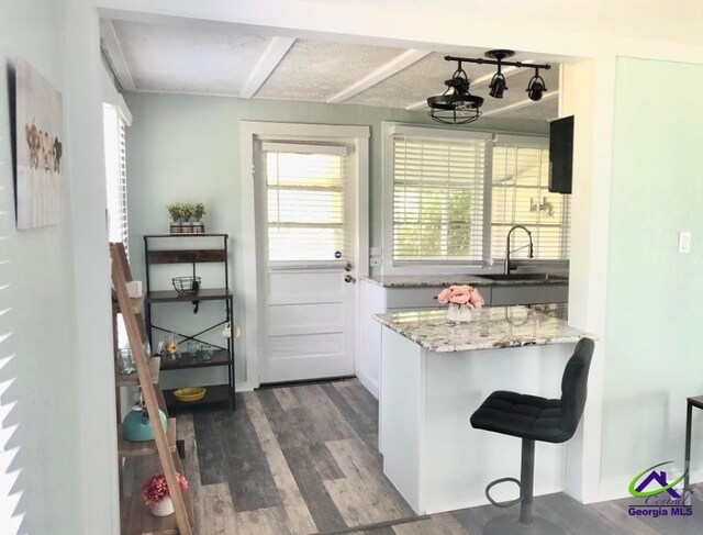 kitchen featuring white cabinetry, hardwood / wood-style flooring, sink, and light stone countertops