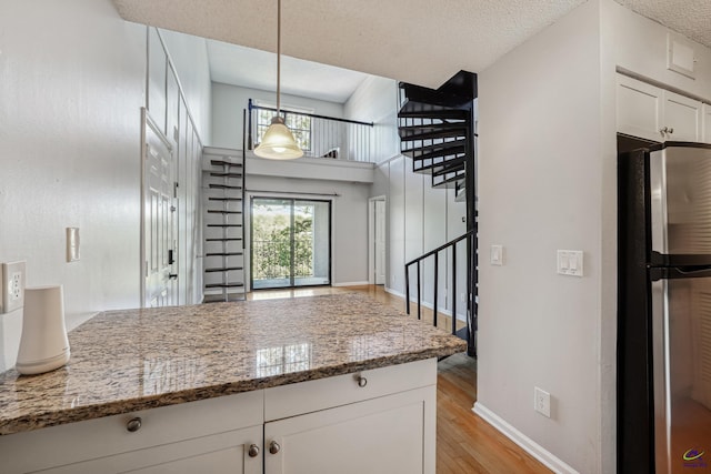 kitchen featuring dark stone counters, stainless steel fridge, pendant lighting, white cabinets, and light hardwood / wood-style floors