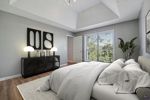 bedroom with a raised ceiling, a textured ceiling, and hardwood / wood-style floors