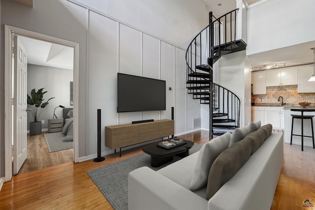 living room with sink, light wood-type flooring, and a high ceiling