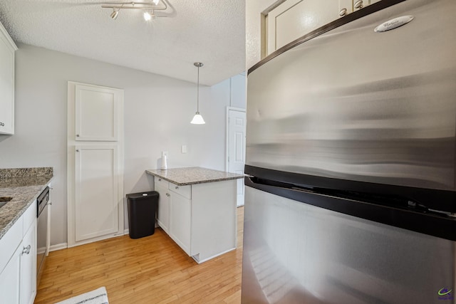 kitchen featuring hanging light fixtures, appliances with stainless steel finishes, white cabinetry, light stone countertops, and light hardwood / wood-style flooring