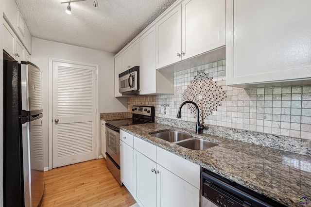 kitchen with appliances with stainless steel finishes, sink, white cabinets, dark stone countertops, and light hardwood / wood-style flooring