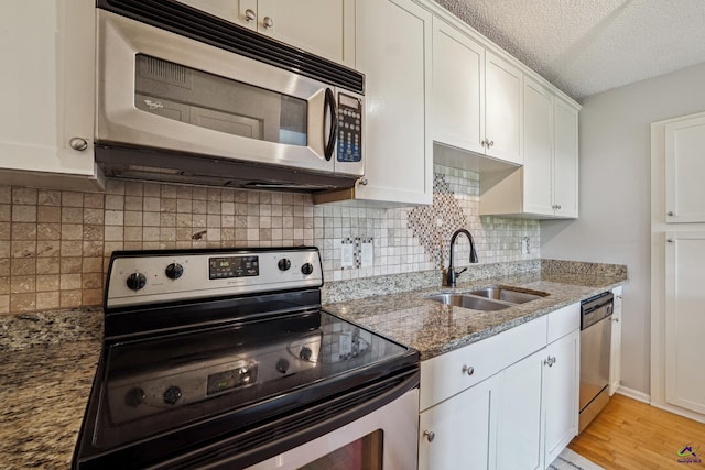 kitchen featuring appliances with stainless steel finishes, sink, stone countertops, a textured ceiling, and white cabinetry