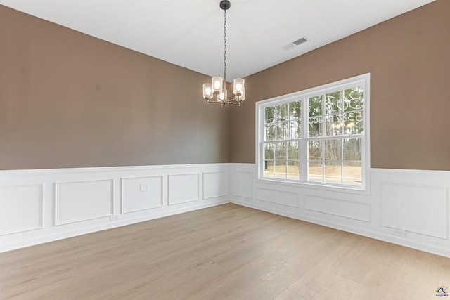 empty room featuring light wood-style floors, visible vents, a notable chandelier, and a wainscoted wall