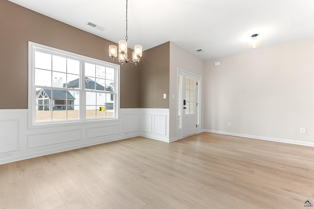 unfurnished room featuring a decorative wall, a wainscoted wall, visible vents, light wood finished floors, and an inviting chandelier