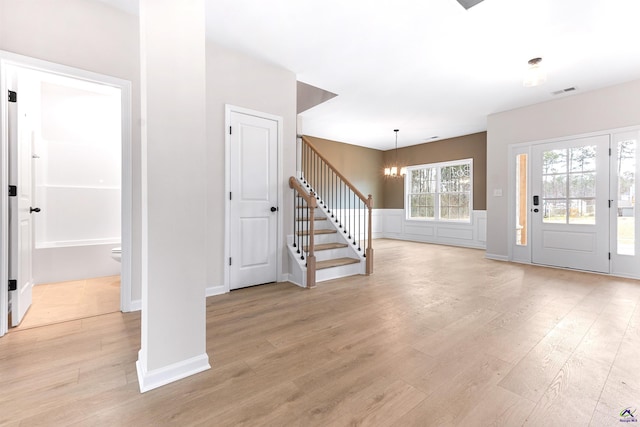 foyer featuring a chandelier, visible vents, light wood-style floors, stairs, and wainscoting