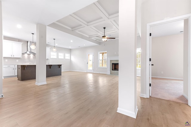 unfurnished living room with ceiling fan, light wood-type flooring, coffered ceiling, and baseboards