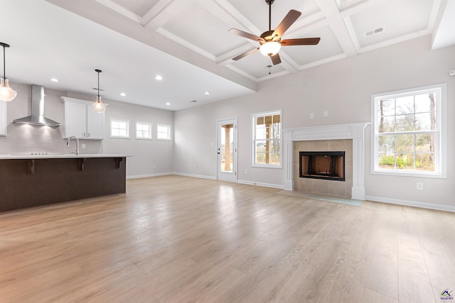 unfurnished living room with visible vents, light wood-style flooring, a tiled fireplace, coffered ceiling, and baseboards