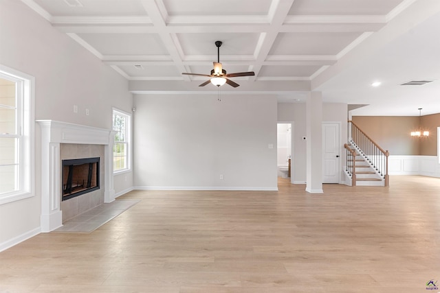 unfurnished living room with coffered ceiling, light wood-style flooring, stairway, a fireplace, and ceiling fan with notable chandelier