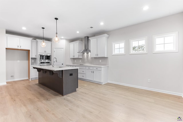 kitchen featuring a breakfast bar area, stainless steel microwave, light countertops, wall chimney range hood, and a sink