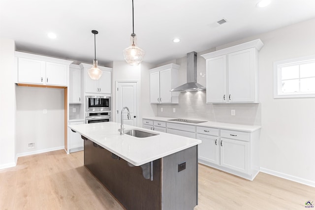 kitchen with white cabinets, wall chimney exhaust hood, a sink, stainless steel appliances, and backsplash