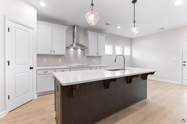 kitchen with a breakfast bar, a center island with sink, light countertops, a sink, and wall chimney exhaust hood