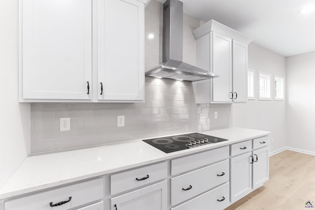 kitchen featuring light wood-style flooring, black electric cooktop, white cabinets, wall chimney range hood, and backsplash