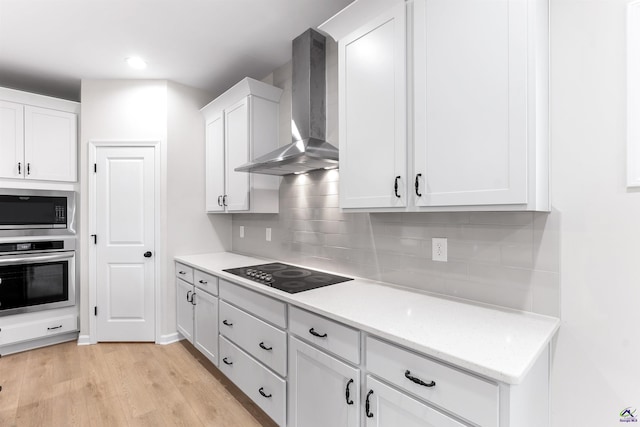 kitchen with light wood-style flooring, appliances with stainless steel finishes, wall chimney range hood, white cabinetry, and backsplash