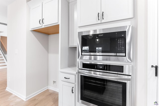 kitchen with oven, white cabinets, light countertops, built in microwave, and light wood finished floors